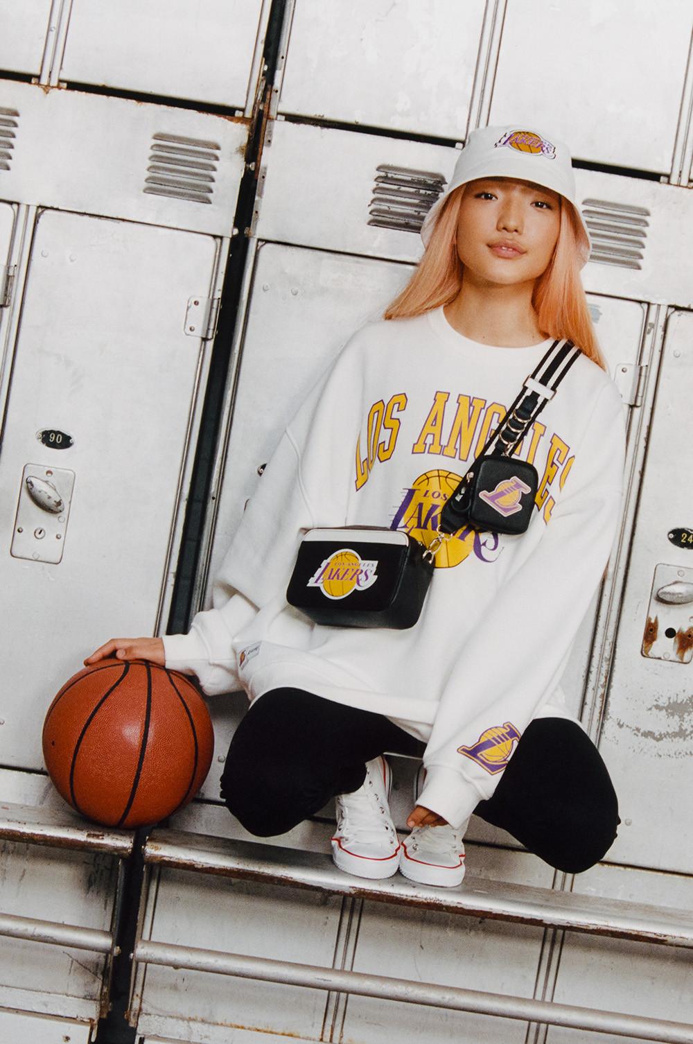 Model wears white long sleeved NBA Lakers tshirt, with matching bucket hat and black crossbody bag