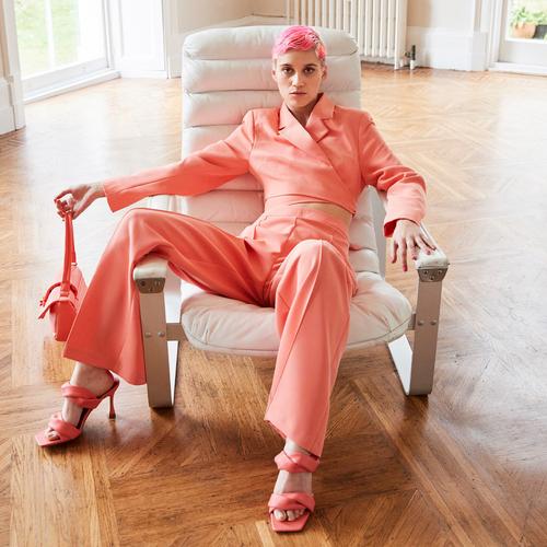 mannequin portant un tailleur pantalon rose avec des chaussures à talons et un sac rose assortis