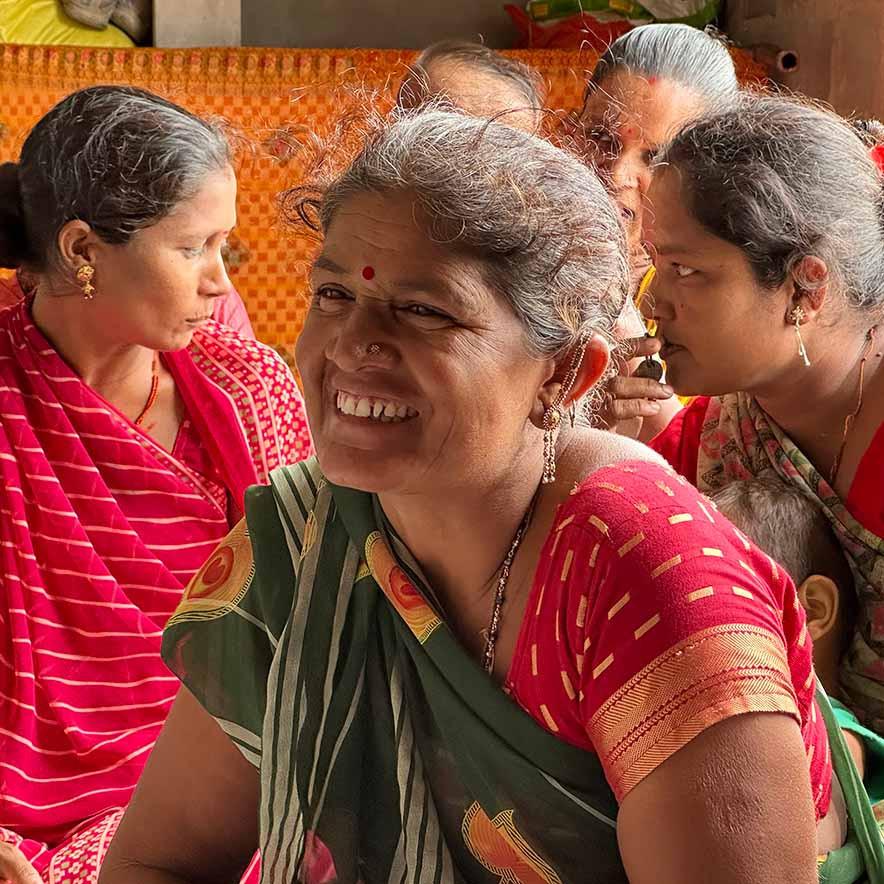 A farmer smiling, sat with other farmers chatting.