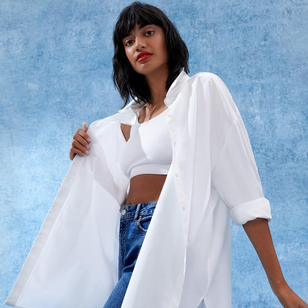 Model wears crisp white shirt, white crop top and blue jeans