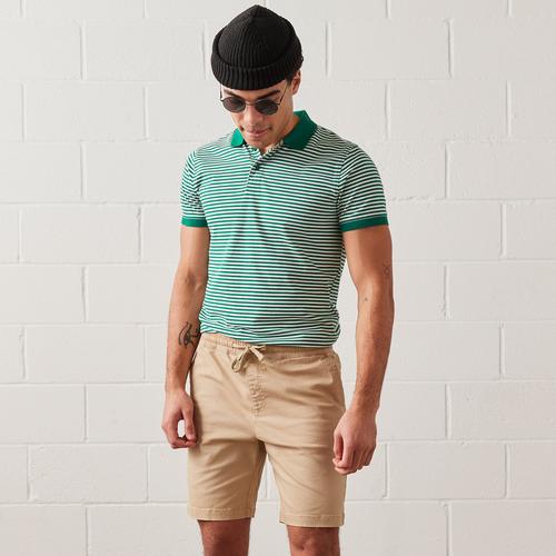 Model wears beige shorts and green polo shirt, with sunglasses