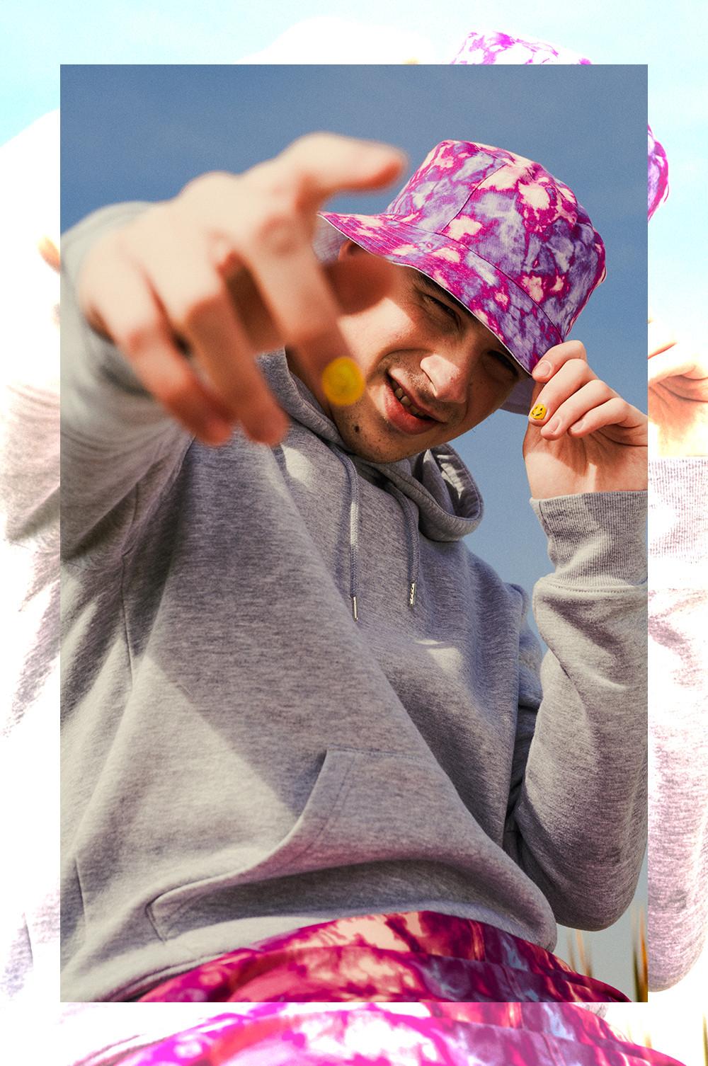 Man wearing pink tie dye shorts and bucket hat with a grey hoodie