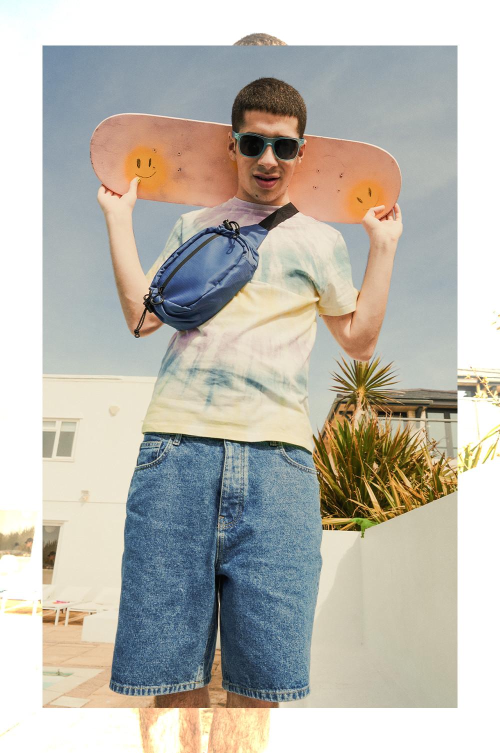 Man wearing tie dye tee, denim shorts and accessories