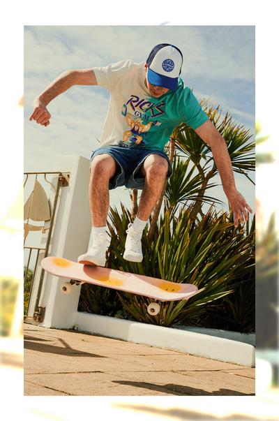 Man wearing cap, denim shorts, graphic tee on a skateboard
