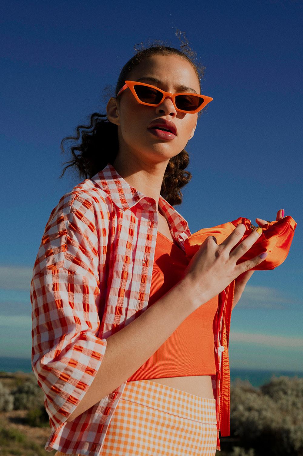 Model wears orange cami top, with orange gingham shirt and flares