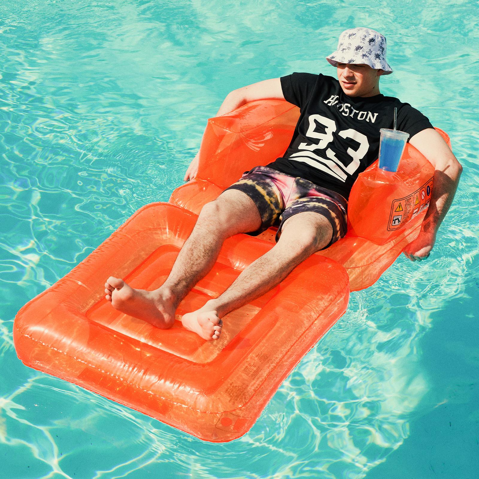 Man lying on lilo in the pool wearing a bucket hat, black Houston tee and tie dye shorts