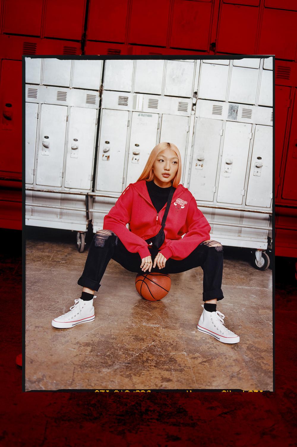 Model wears red NBA Bulls zip up hoodie, black NBA bulls bum bag and black ripped jeans