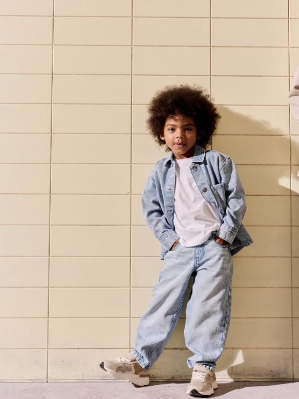 Child wearing grey and blue colour-block hooded jacket with matching dark trousers and blue trainers.