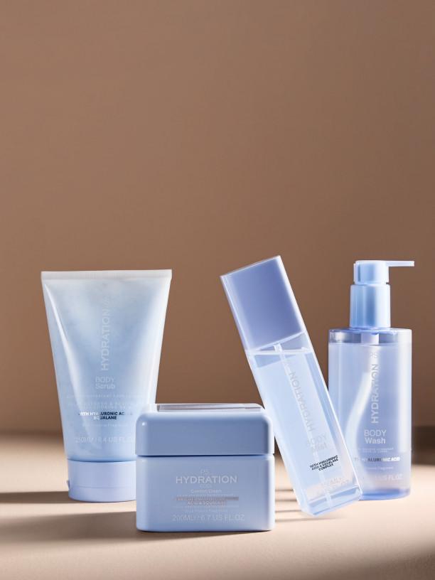 Three PS Cooling body mist bottles in orange, pink and green with water droplets on glass shelf.