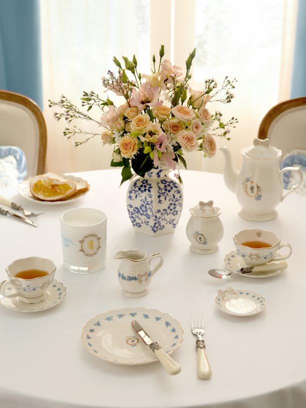 Elegant bedroom featuring white textured bedding, pleated pendant light, and wooden bedside table with pink flowers.