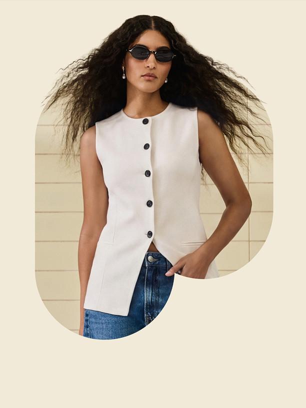 Person wearing mauve sports bra with black sweater raised above head, against pink background with white oval shape.