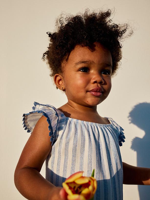 Child wearing grey and blue colour-block hooded jacket with matching dark trousers and blue trainers.