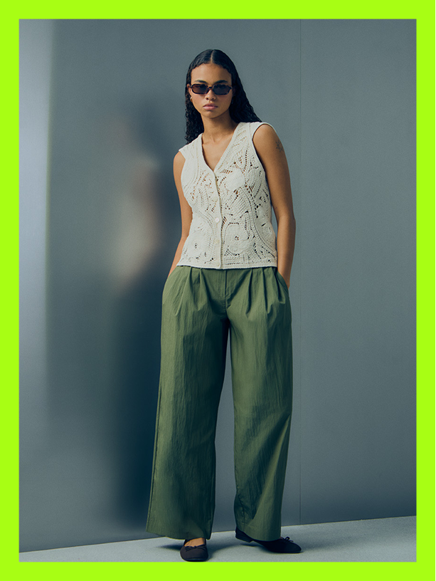 Woman wearing sunglasses, cream embroidered sleeveless top and olive green wide-leg trousers.