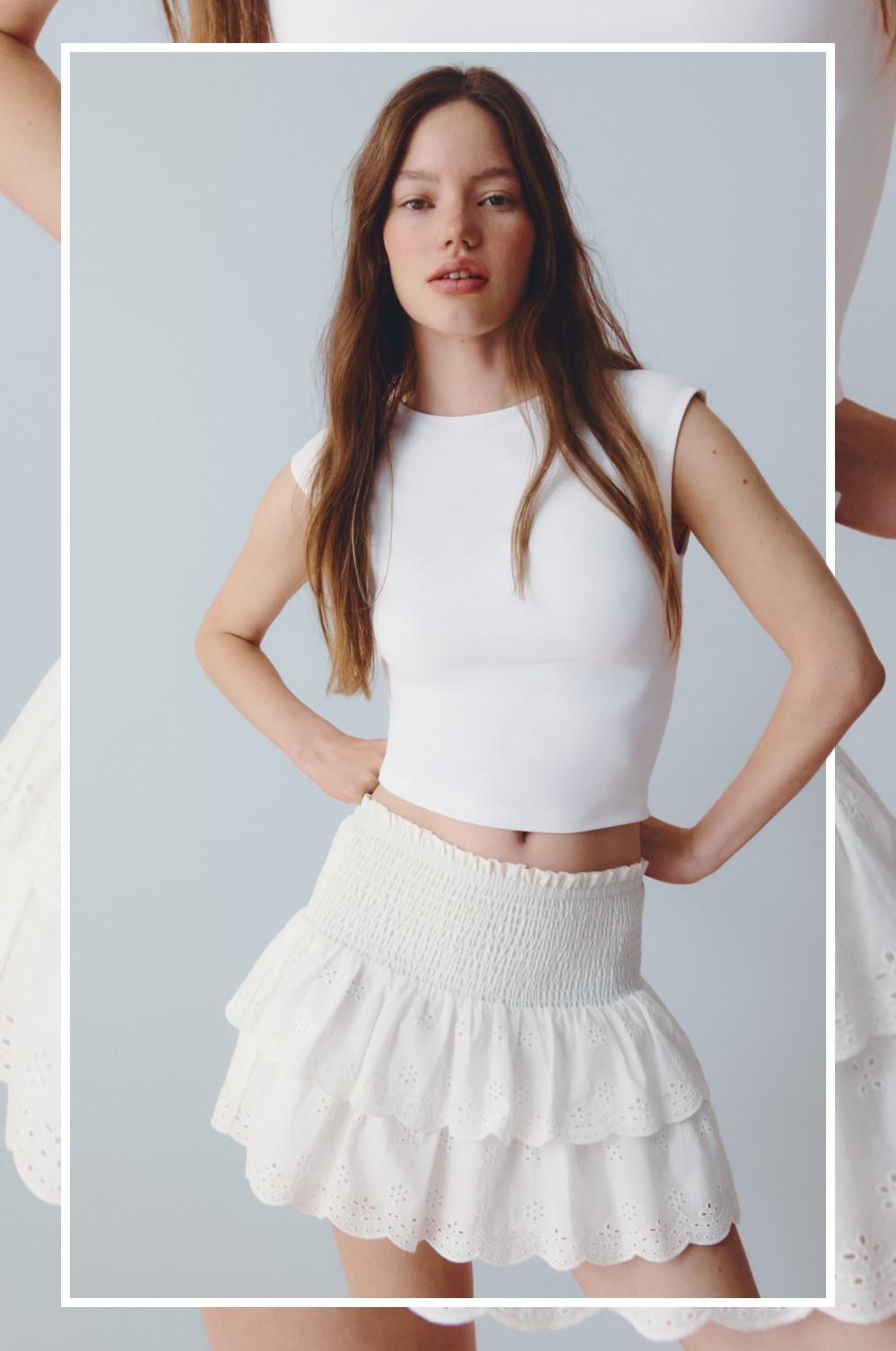 Modelo posa con las manos en las caderas con una camiseta corta sin mangas y una minifalda a capas con detalles en bordado inglés.