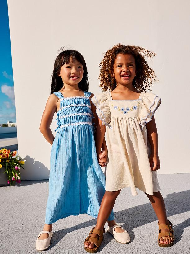 Child in pink tracksuit demonstrating martial arts stance with pink trainers against white background.