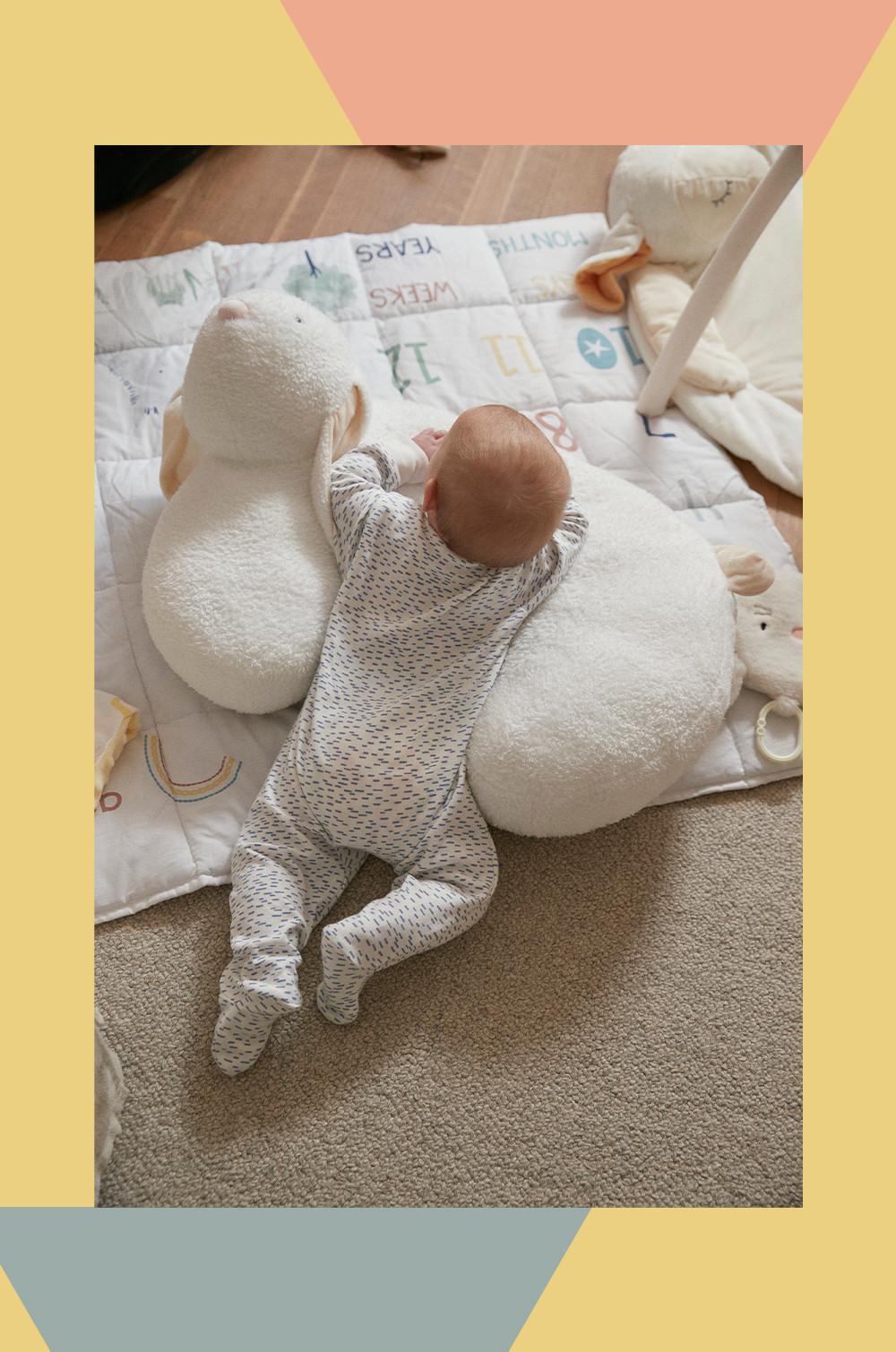 Baby in Bauchlage auf einem weißen Hasen-Sitzkissen und einer Kuscheldecke