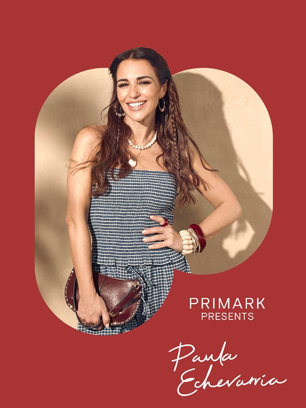 Woman smiling in striped strapless dress holding clutch bag, wearing pearl necklace and gold jewellery.