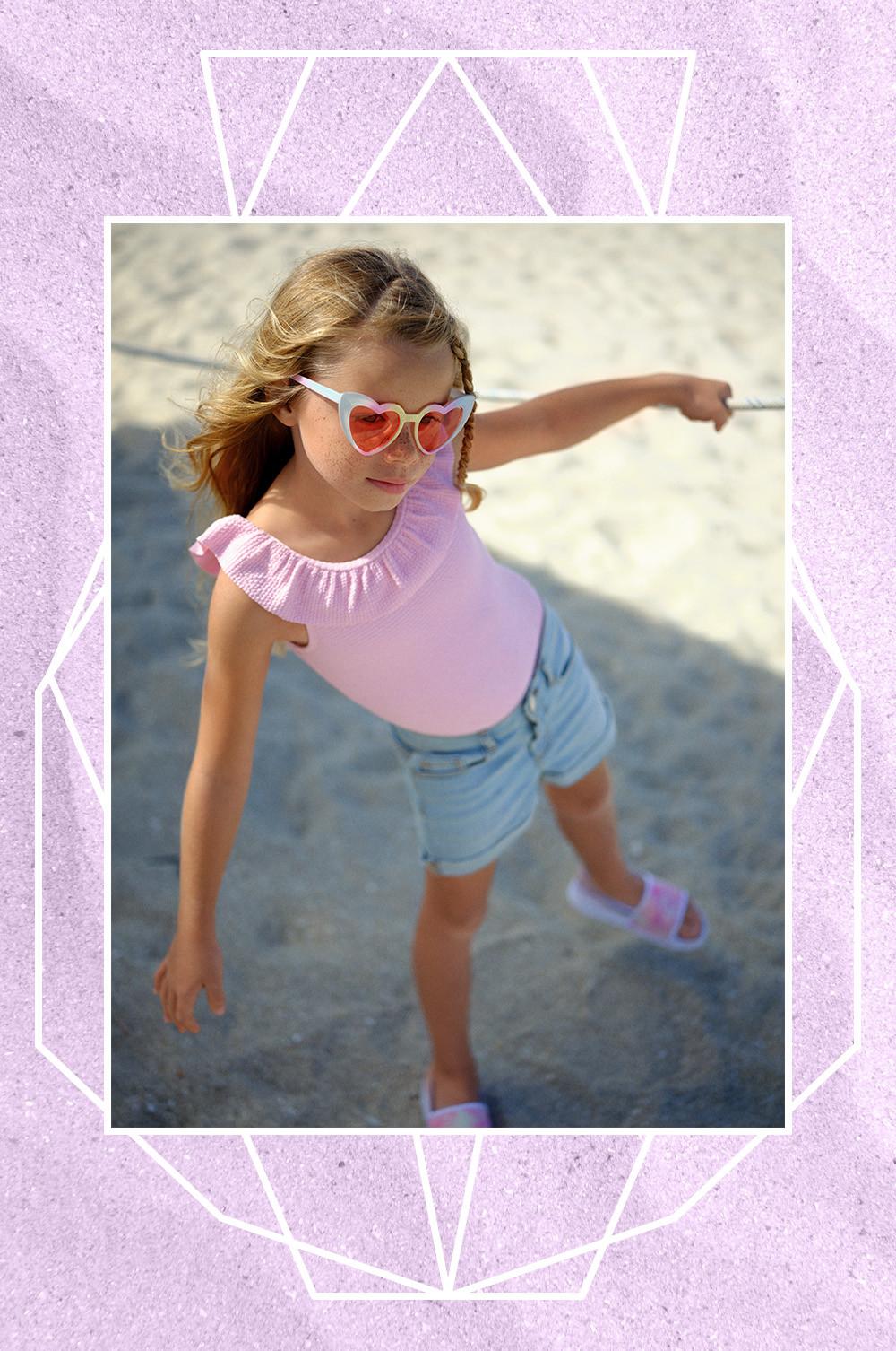 Child in denim shorts, textured pink swimsuit, sunglasses