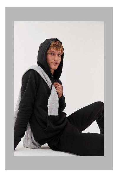 Model in zwart joggingpak met een grijze hoodie over de schouders