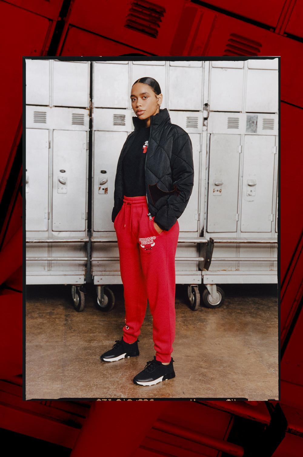 Model wears red NBA Bulls joggers, with black NBA Bulls crop top and a plain black padded jacket