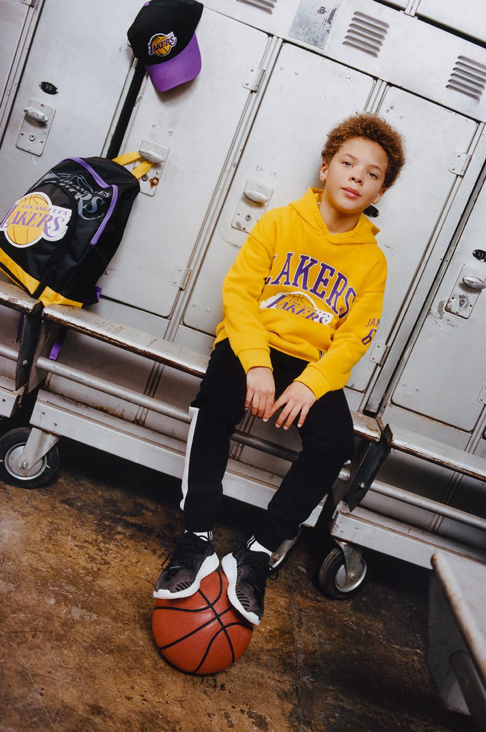 Child wears NBA Lakers yellow hoodie, paired with black Lakers joggers, Lakers cap and backpack