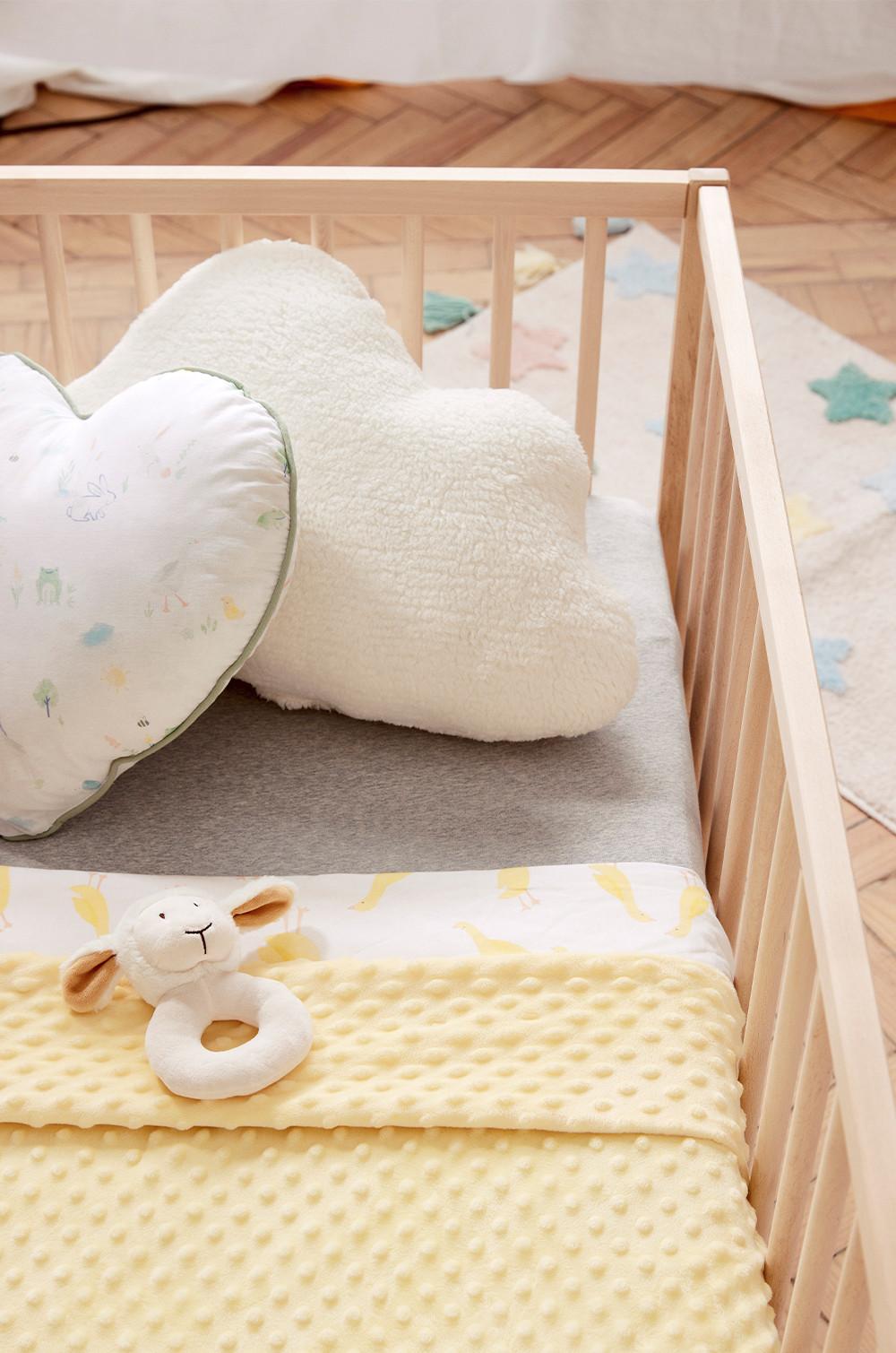 Baby crib set up with cot sheet, pillows and baby rattle