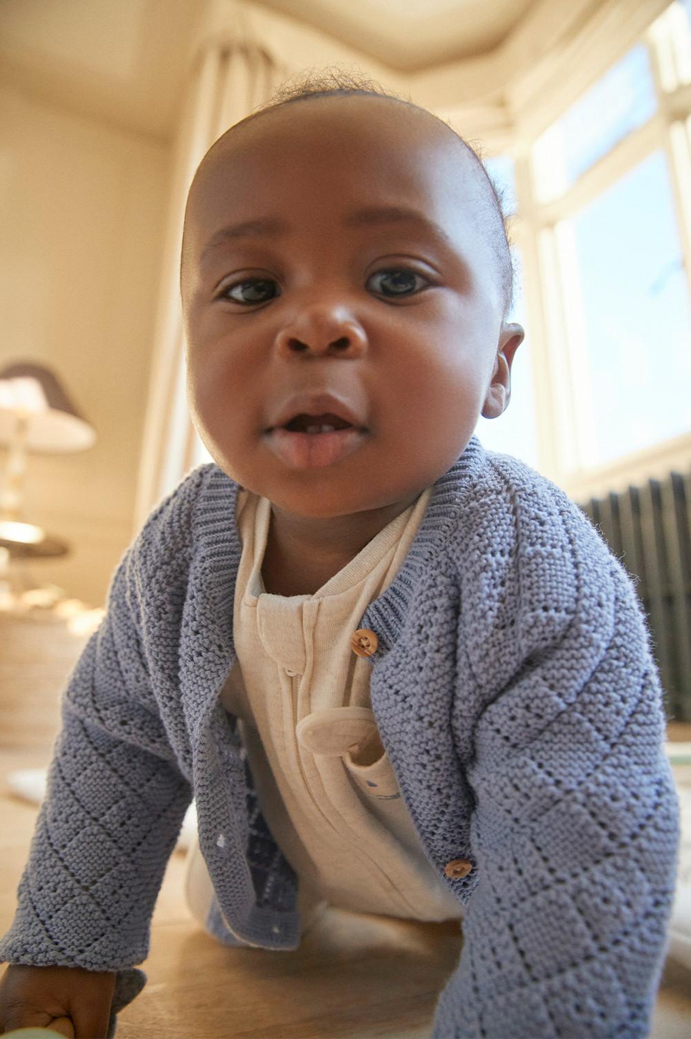 Baby wears white sleep-suit with lilac cardigan