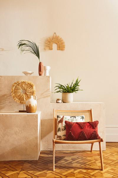 Disposición de estantería empotrada con jarrones rústicos y plantas artificiales, y silla de ratán