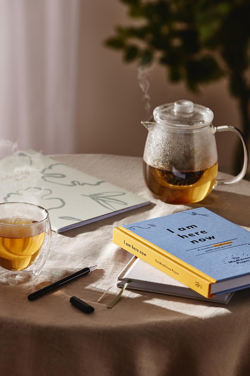 Decoración de mesa con diario de bienestar y tetera de cristal con taza a juego