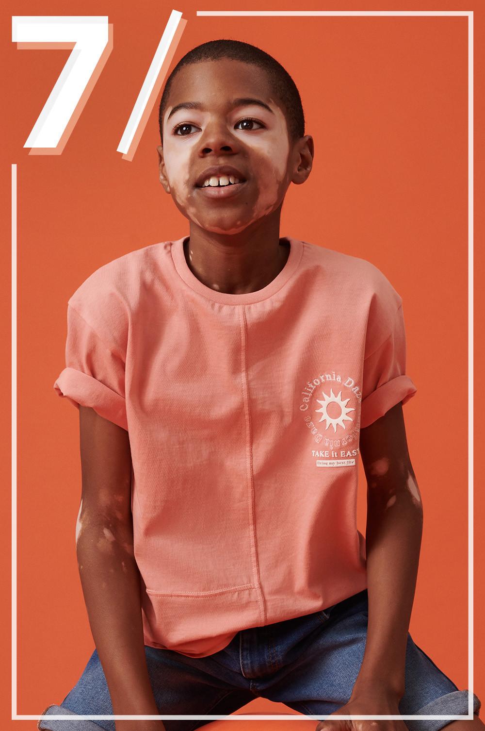 Kind in orangefarbenem T-Shirt und Jeansshorts