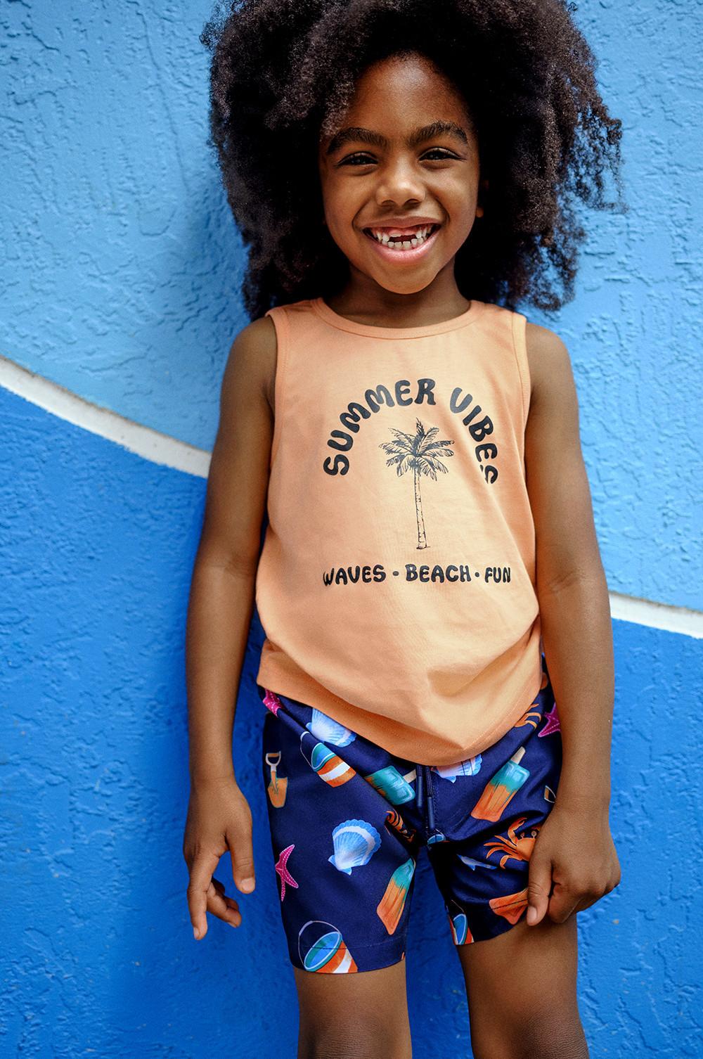 Child wearing patterned swim shorts and orange graphic tee