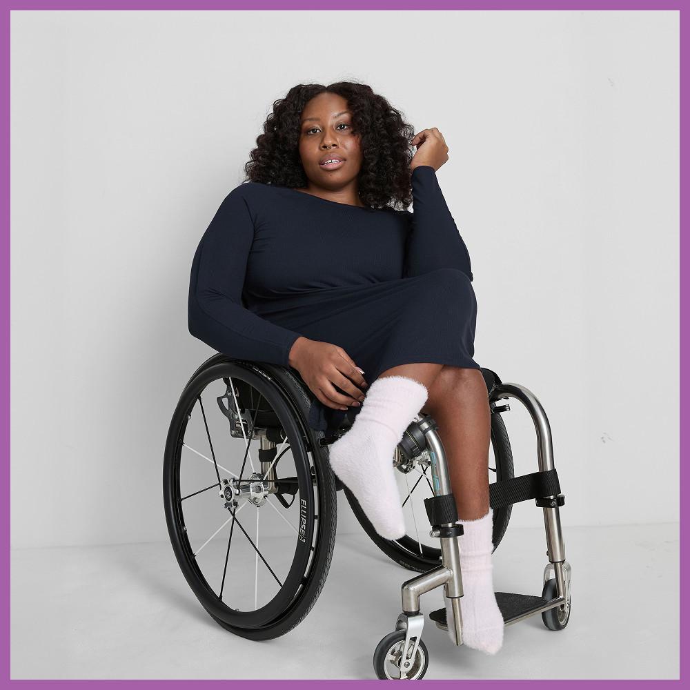 Model with curly hair wearing a navy long-sleeved dress, seated in a wheelchair.
