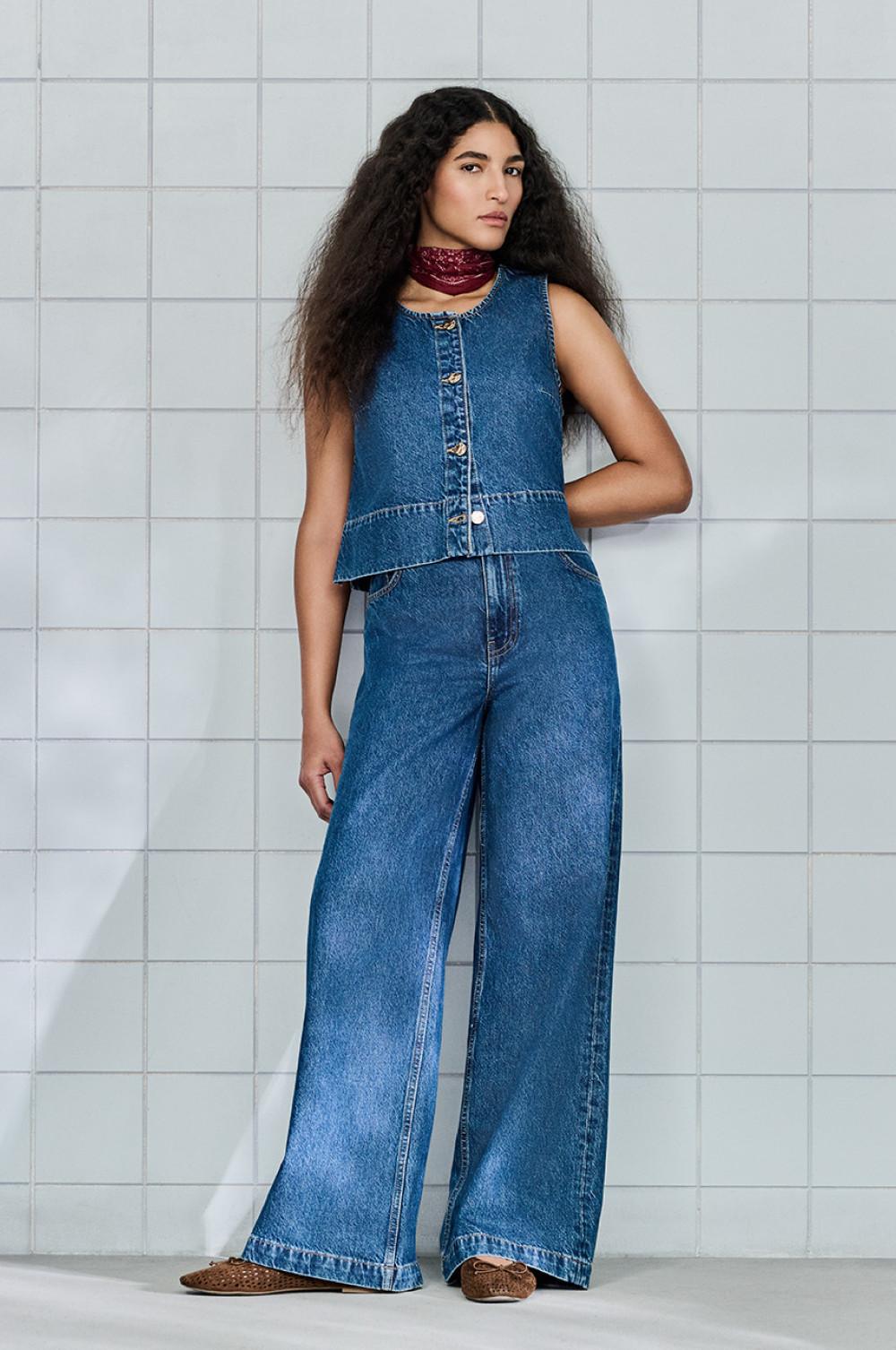 Denim outfit van een mouwloze blouse met knoopsluiting en een wijde spijkerbroek gecombineerd met een rode sjaal.