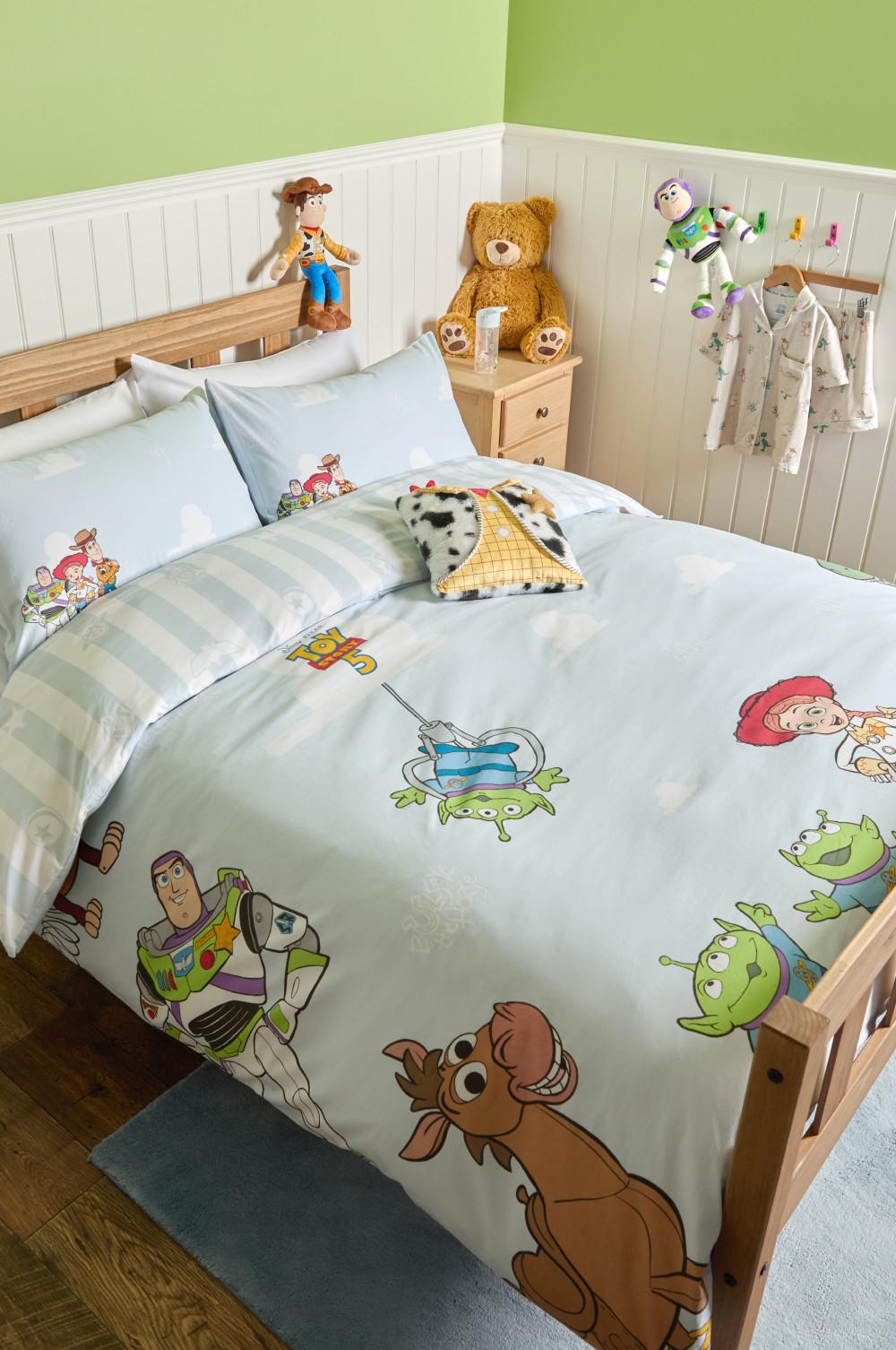 Toy Story themed children's bedding set with character prints on duvet and pillowcases in a wooden bed.