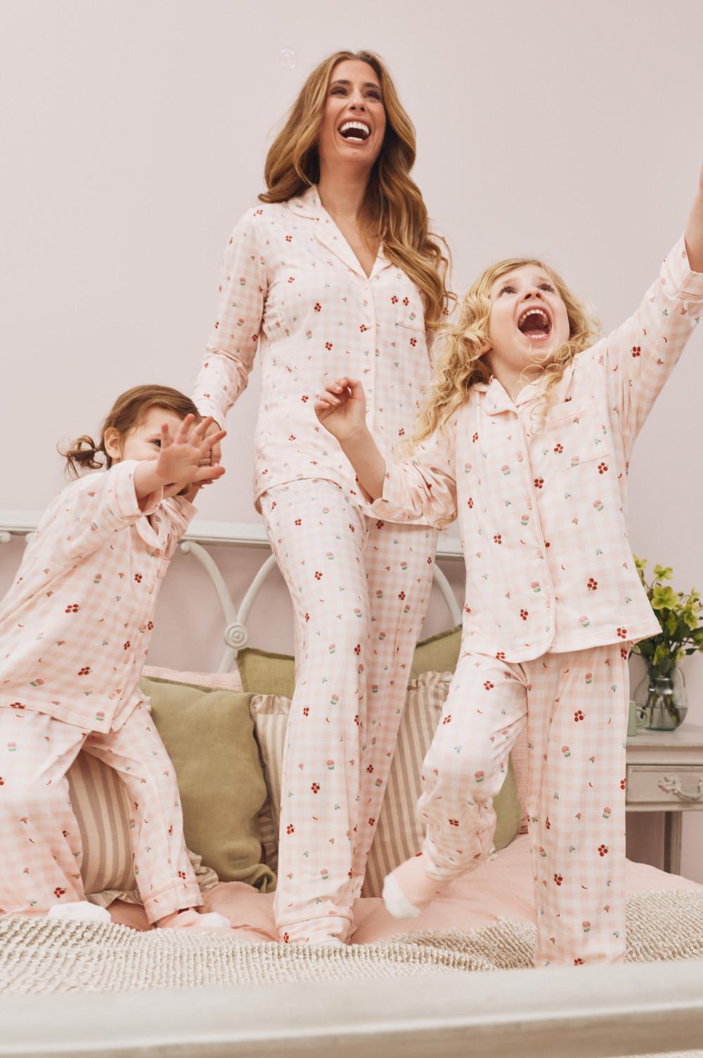 Family wearing matching pink floral pyjamas jumping excitedly on a bed in a bedroom setting.