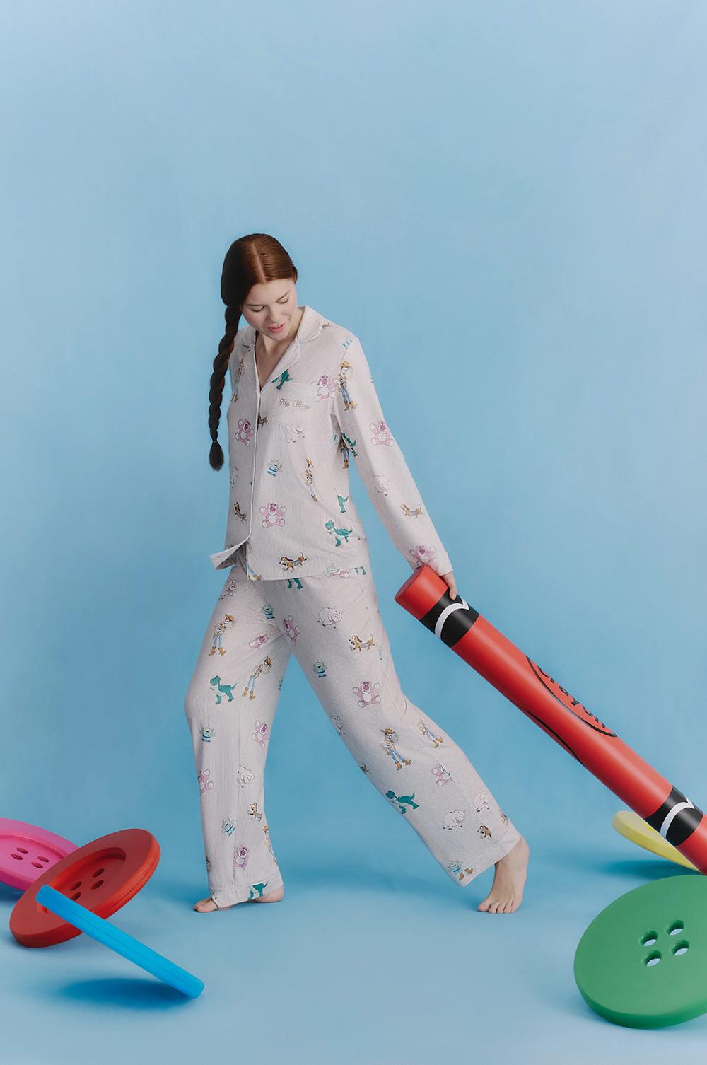 Model wearing white pajamas with colorful dog print, holding an oversized red crayon.