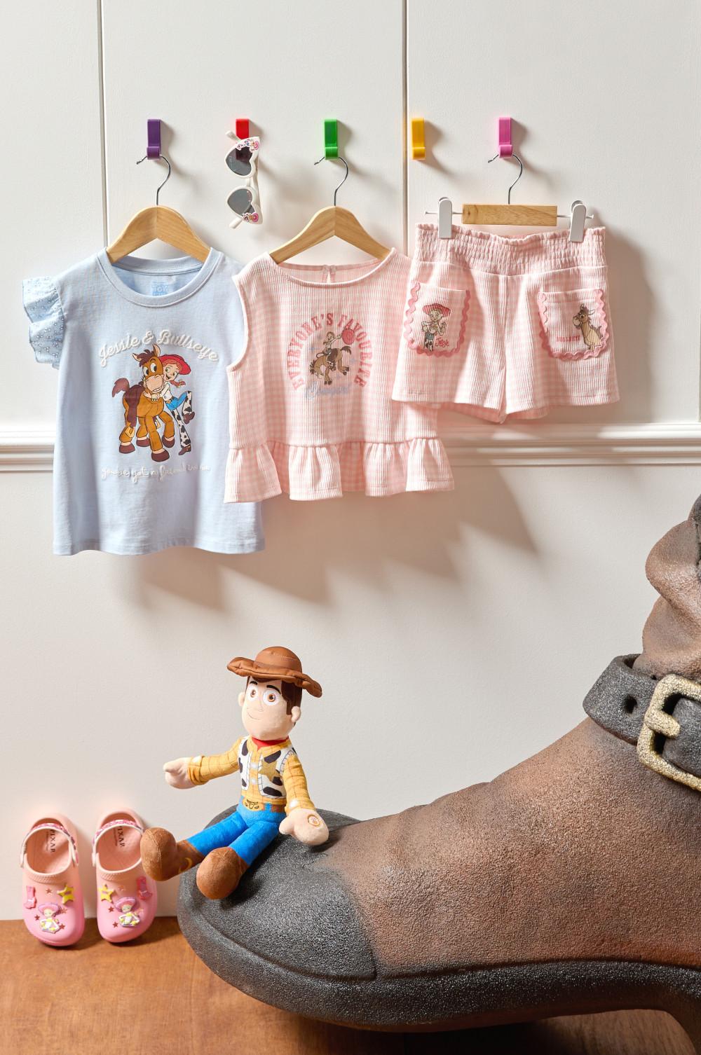 Children's Toy Story pajamas hanging on wooden hangers with matching shorts and Woody toy displayed below.