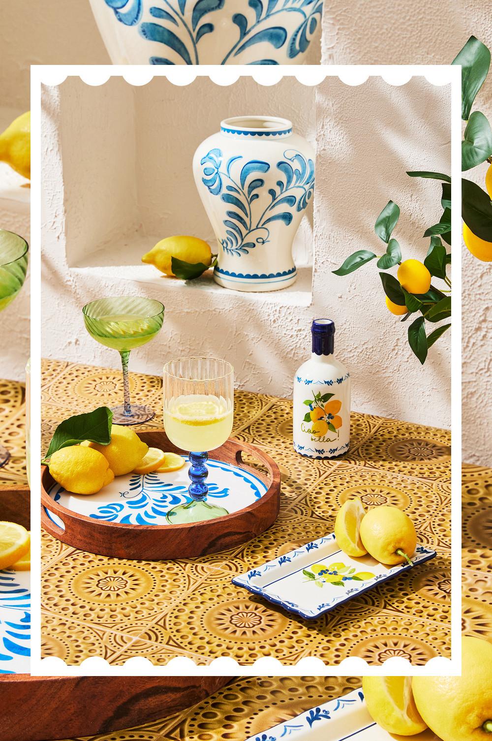 Mediterran inspirierte Tischdekoration aus blauer Keramik mit Blumenmuster, Limoncello-Flasche, Cocktailgläsern und frischen Zitronen.