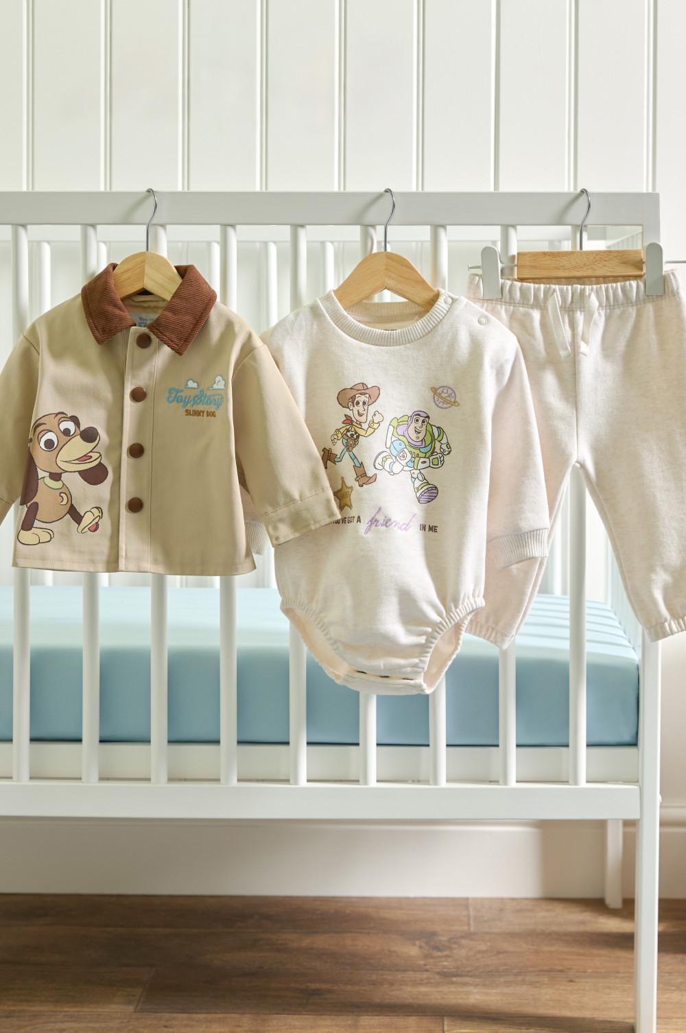 Three-piece baby outfit set hanging on cot rail featuring Disney characters from Toy Story and Slinky Dog.