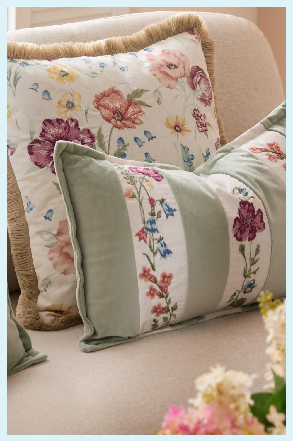 Decorative cushions with floral embroidery patterns on a beige sofa, featuring sage green and white designs.