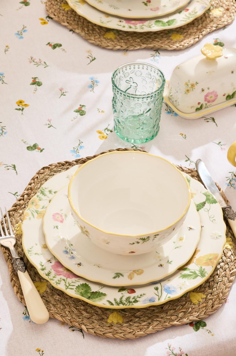 Floral dinnerware set with white and gold-rimmed bowl and plates on woven placemats, with mint glass and butter dish.