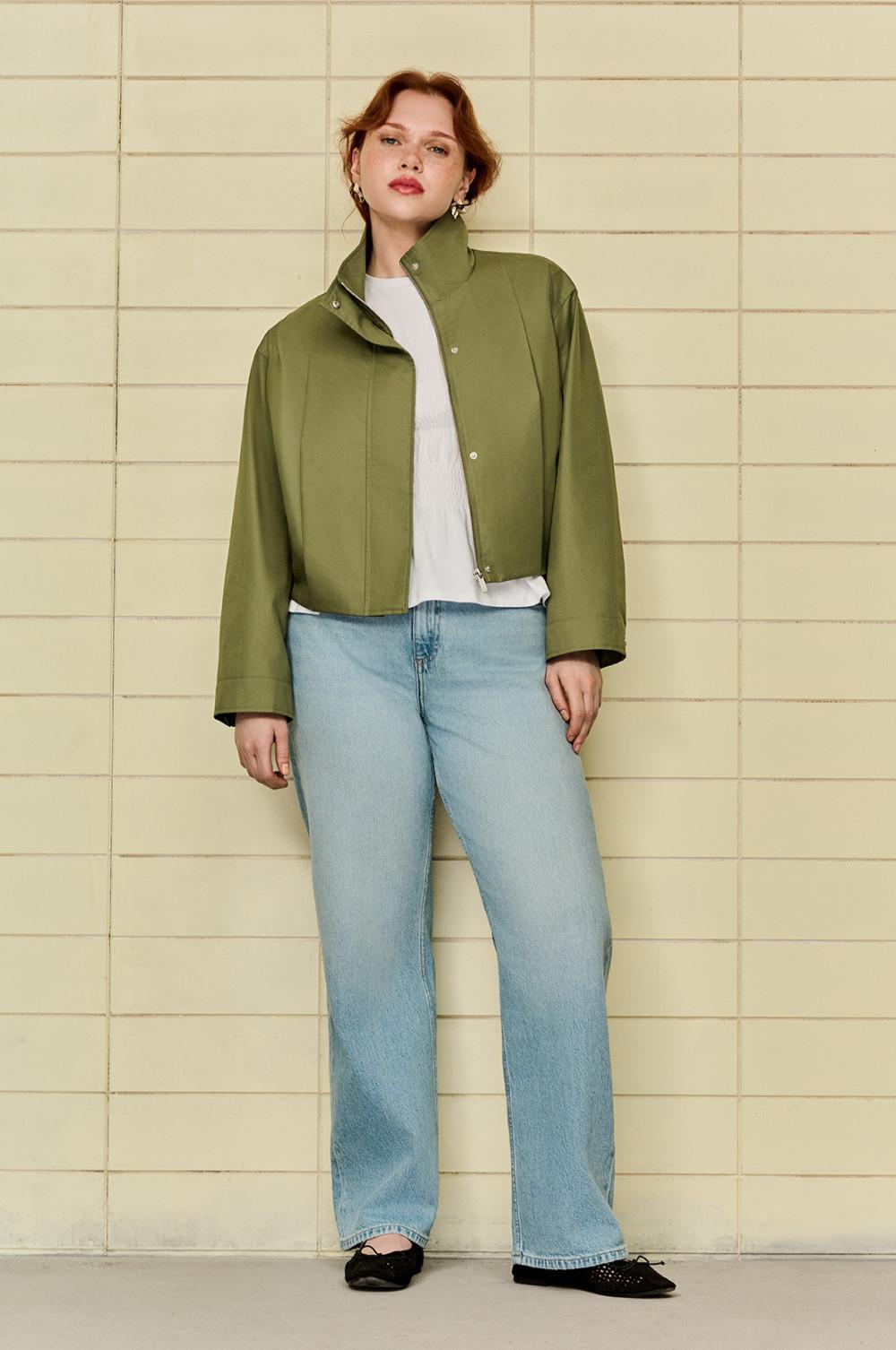 Kort olijfgroen jack met hoge kraag gedragen met een wit topje en een lichte spijkerbroek.