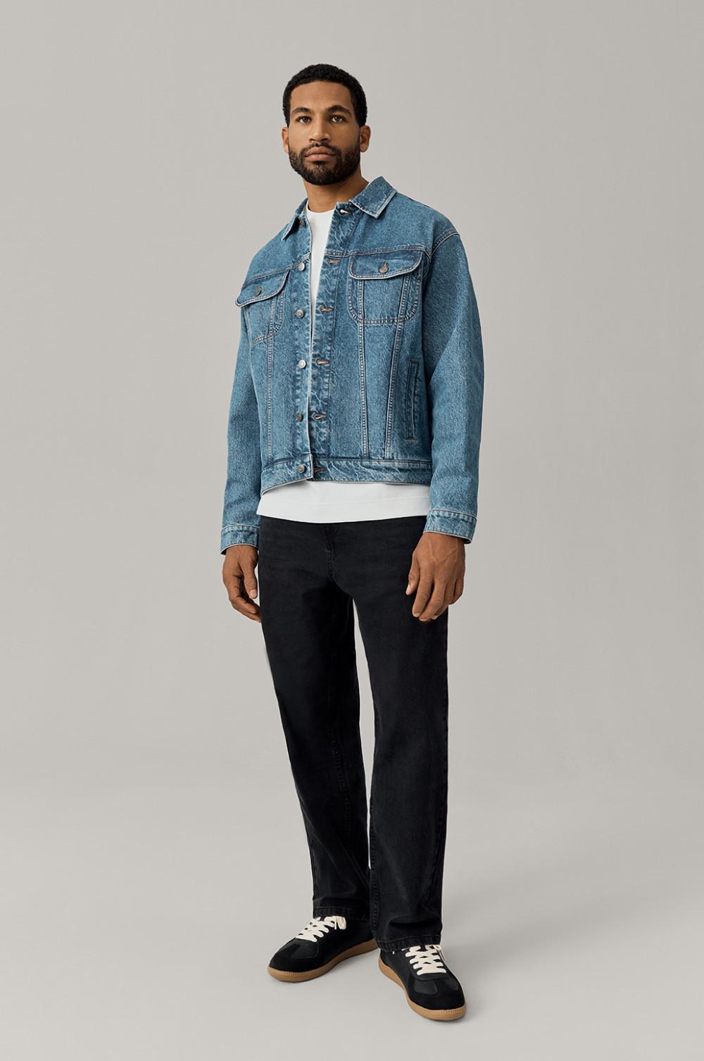 Person wearing classic blue denim jacket over white T-shirt with black pants and sneakers.