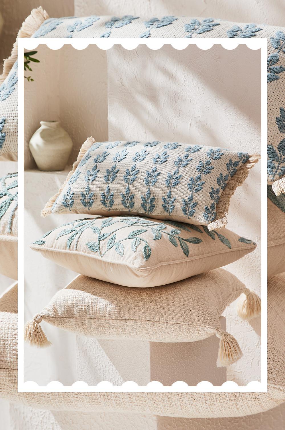 Drei dekorative Kissen mit blauer Blumenstickerei und Quastendetails auf naturfarbenem Leinenstoff.