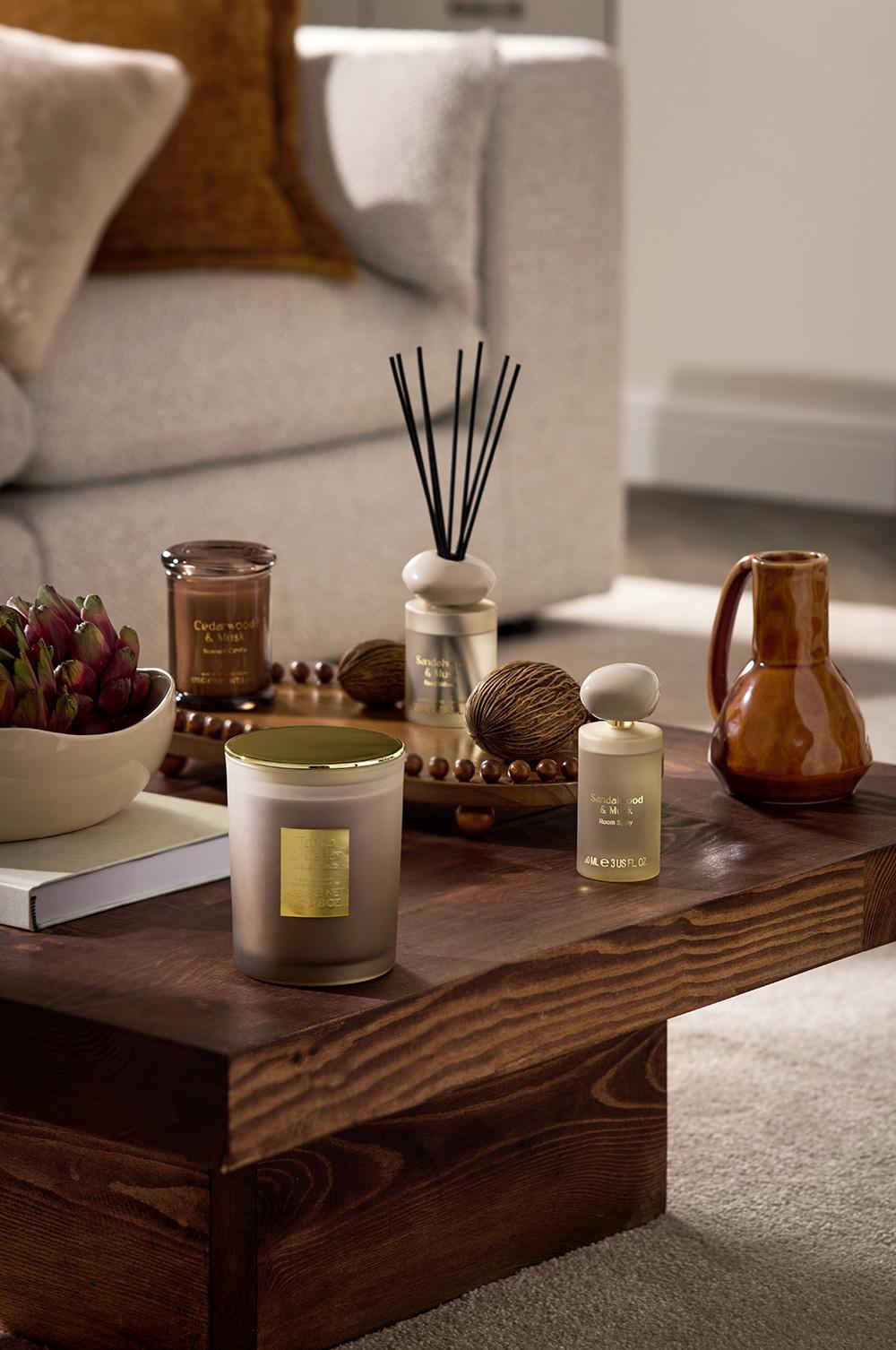 Home fragrance collection with scented candles, reed diffuser and decorative items on wooden coffee table.