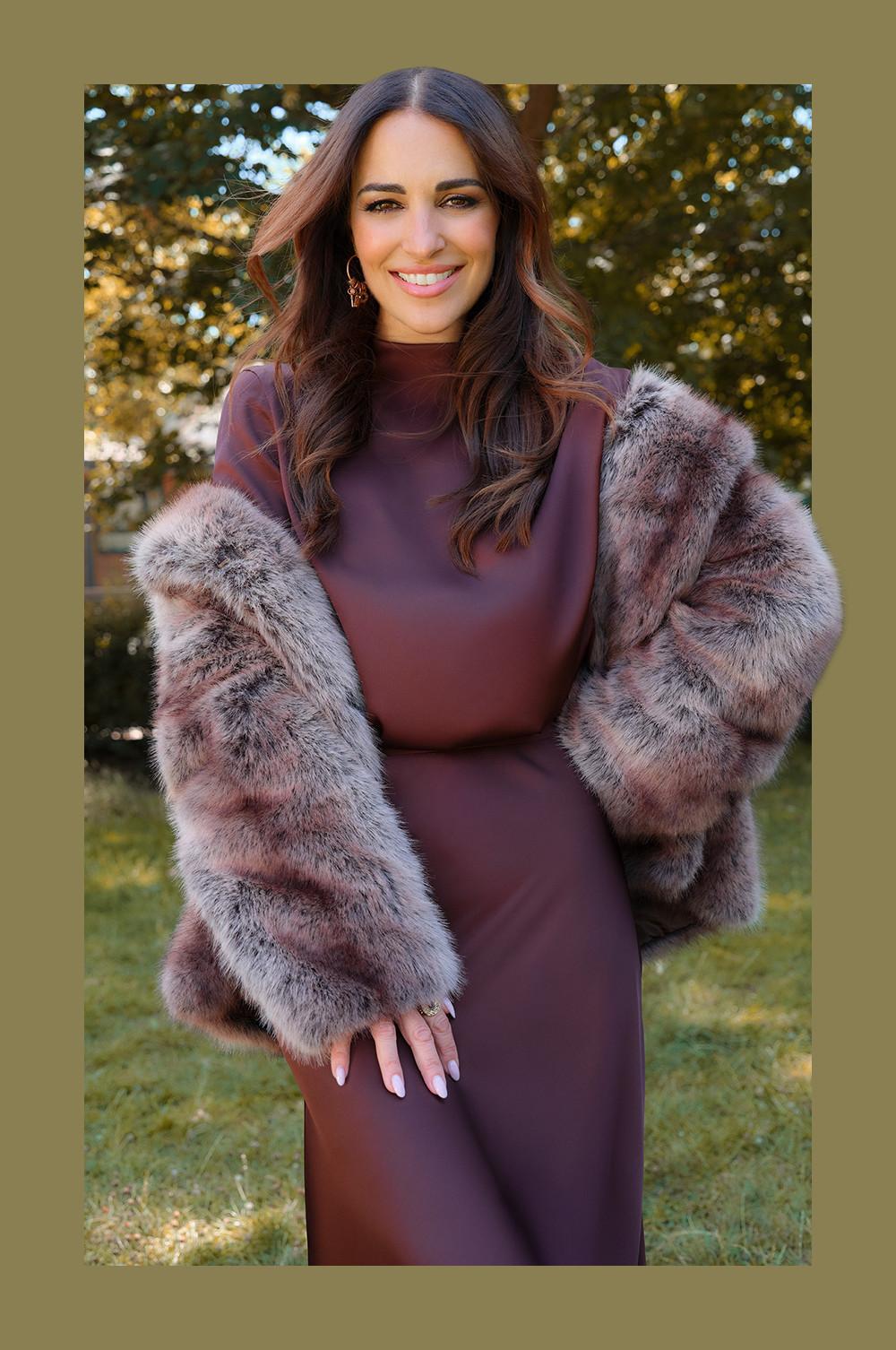 Personne portant une robe bordeaux avec une veste en fausse fourrure luxueuse dans des tons rose pâle et gris.