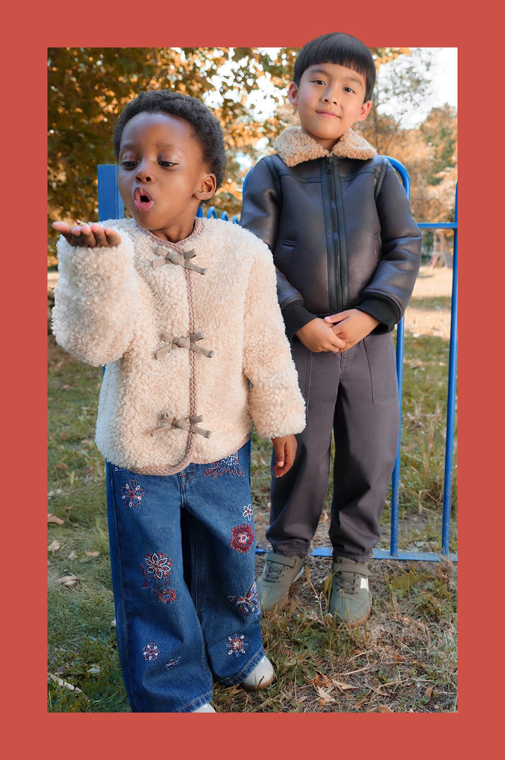 Deux enfants portant des vestes d’hiver en plein air, l’un avec un manteau sherpa crème à gros boutons, l’autre avec une veste en simili cuir marron.