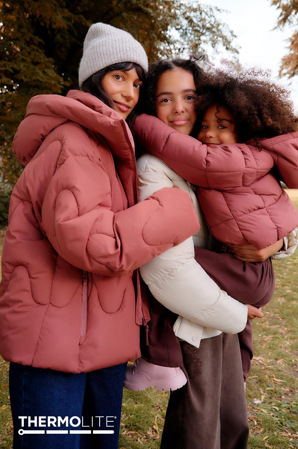 Three people wearing coordinating dusty pink and white puffer jackets outdoors in autumn. THERMOLITE logo visible.