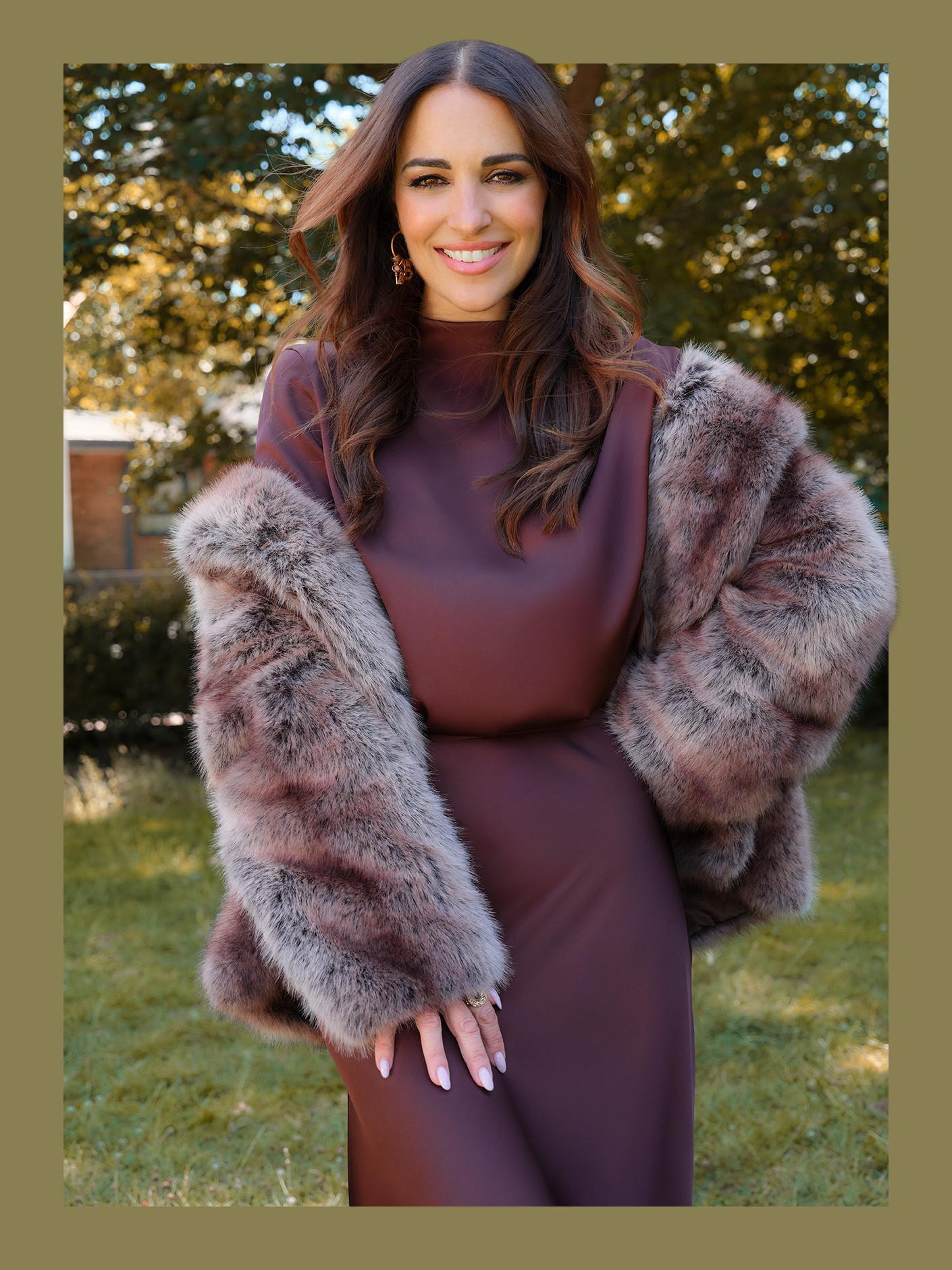 Person wearing burgundy dress with textured faux fur jacket in autumn outdoor setting.