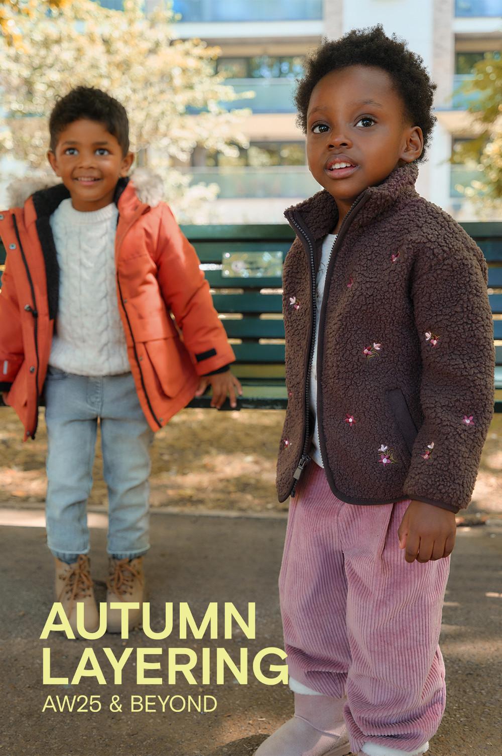 Two children wearing autumn outerwear - brown teddy jacket with pink trousers and orange coat with jumper and jeans.